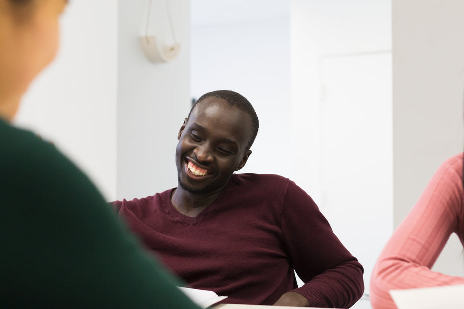 Black man in plum shirt smiles while talking to a small group