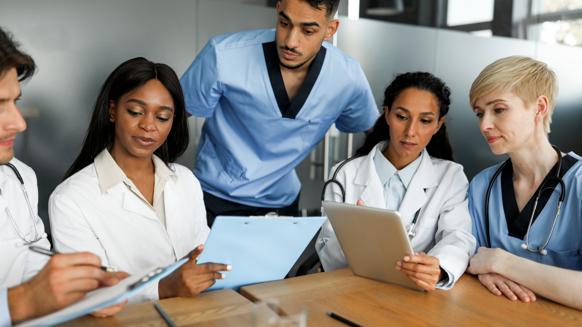 Professional international team of doctors men and women in uniforms sitting at table using digital tablet taking notes as medical externships 